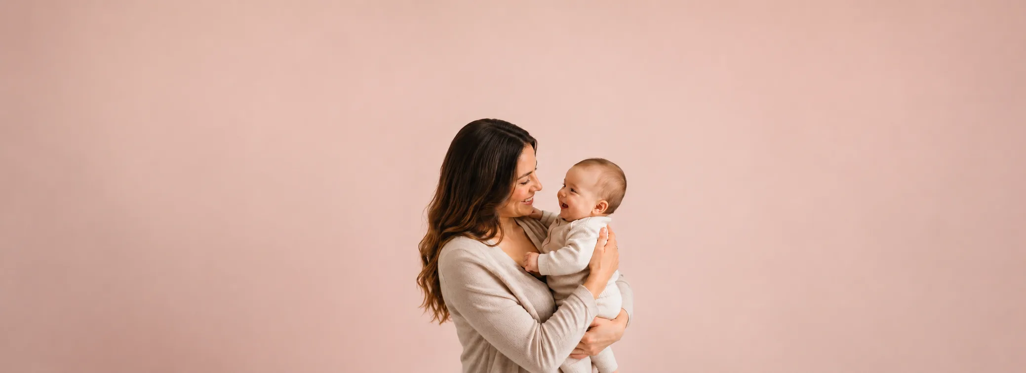 Mãe sorrindo com bebê no colo diante de parede rosa